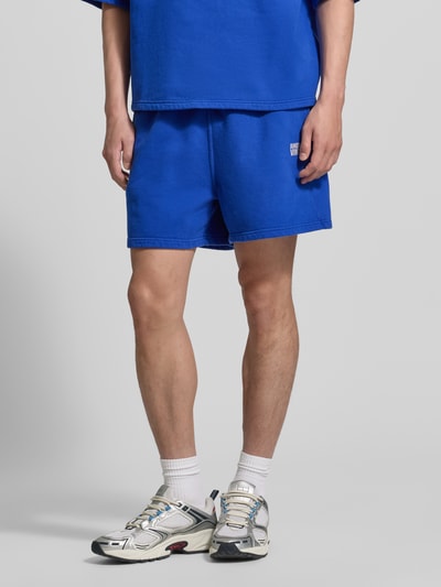 Männermodel trägt Shorts mit Logo Modell 'PLIZZY' von American Vintage in Blau, Reine Baumwolle, Relaxed-Fit, Vorderansicht Ganzkörperansicht.