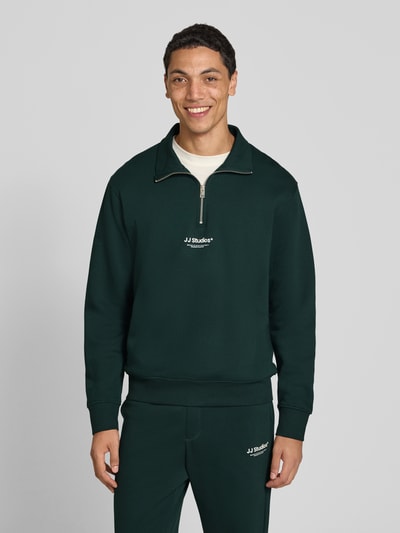 Männermodel trägt Regular Fit Sweatshirt aus Baumwoll-Mix Modell 'Soho' von JACK & JONES in Dunkelgrün mit Logo-Print, Ganzkörperansicht von vorne.
