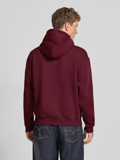 Męski model nosi Relaxed Fit Hoodie aus Baumwoll-Mix mit Logo-Stickerei od REVIEW, kolor bordowy, wykończenia prążkowane, Kieszeń kangurka, Kaptur z tunelem, długi rękaw, Długość tyłu w rozmiarze M: 67 cm, Długość rękawów: 65 cm, Ganzkörperansicht Rückansicht