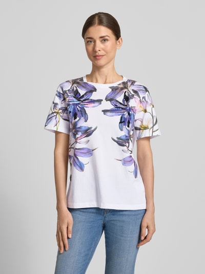 Frauenmodel trägt T-Shirt im Allover-Look mit Pailletten von Marc Cain, Damen T-Shirt aus Reine Baumwolle, Regular-Fit, Rundhalsausschnitt, Rückenlänge bei Größe 36: 59 cm, florale Muster in Lila, Weiß und Schwarz, glatte Textur, Ganzkörperansicht von vorne.