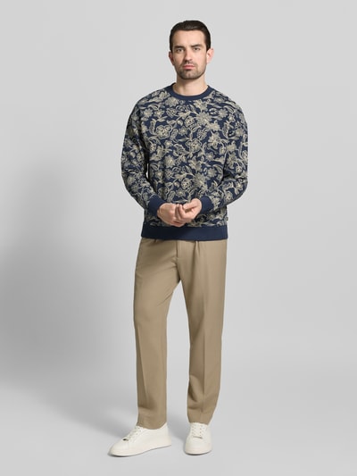Mannelijk model draagt Sweatshirt im Allover-Look mit Rundhalsausschnitt van Scotch & Soda in blauw met beige dessin, puur katoen, regular fit, all-over look, ruglengte maat M 67 cm, mouwlengte maat M 68 cm. Ganzkörperansicht von vorne.