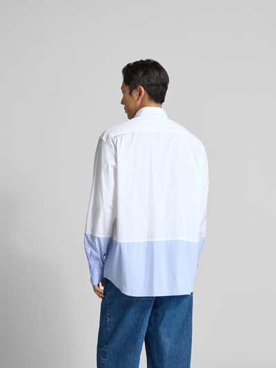 Männermodel trägt Regular Fit Freizeithemd aus Baumwolle von VETEMENTS, farblich zweigeteilt in Weiß und Hellblau, Rückenansicht Ganzkörperansicht. Rückenlänge bei Größe M 83 cm, Schulterbreite 54 cm, Ärmellänge 68 cm, Reine Baumwolle, Durchgehende Knopfleiste, Brusttasche, Langärmeliges Design.