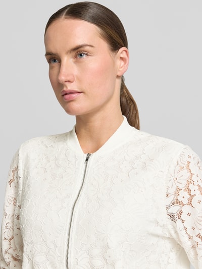 Kobiece model nosi Regular Fit Blouson aus Baumwoll-Mix model 'HONEY' od Vero Moda, florystyczny wzór na całej powierzchni, zamek błyskawiczny, prążkowane zakończenia, kształt kołnierza college, wykończenie: imitacja wykonania na szydełku, mieszanka bawełny, kremowy kolor, faktura koronkowa, z długim rękawem, optyka: wzór na całej powierzchni, zbliżenie na górną część ciała.