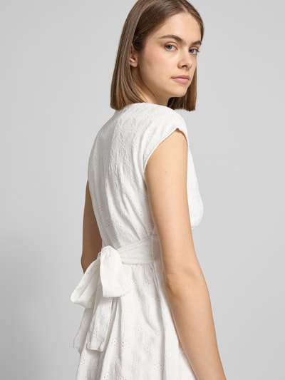 Frauenmodel trägt Kurzes Kleid mit V-Ausschnitt, Lochstickerei und großer Schleife von REVIEW, weißer Material-Mix mit Stretch-Anteil, A-Linie, Rückenlänge 84 cm, Brustweite 42 cm, Ganzkörperansicht Rückansicht.