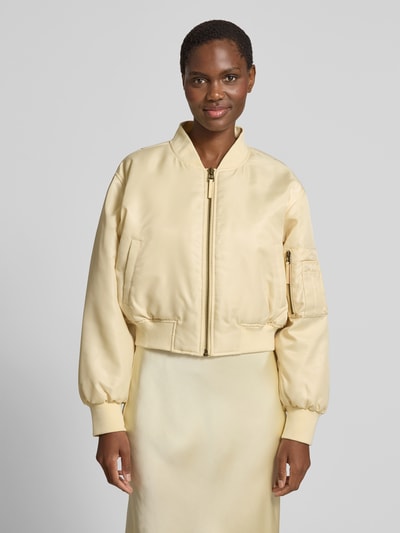 Frauenmodel trägt Bomberjacke mit Stehkragen von Anine Bing in hellem Beige, glänzende Textur, Regular-Fit, Reißverschluss, Eingrifftaschen, elastische Abschlüsse, Rückenlänge bei Größe S 50 cm, Brustweite 60 cm, Ärmellänge 58 cm, Ganzkörperansicht von vorne.
