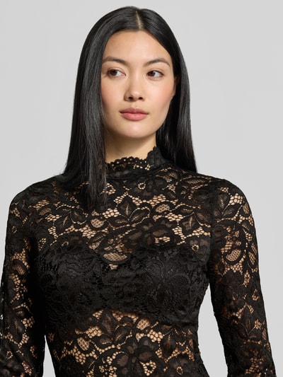 Frauenmodel trägt Slim Fit Longsleeve aus floraler Spitze Modell 'Lacey' von YAS in Schwarz, Stehkragen, semitransparentes Design, Nahaufnahme Oberkörper.