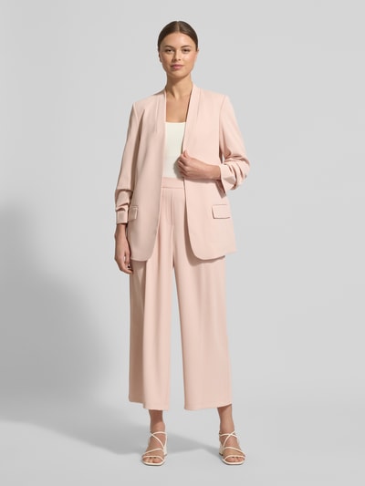 Frauenmodel trägt Blazer mit Pattentaschen von Jake*s Collection in zartem Rosaton, Material-Mix mit Stretch-Anteil, lockerer Schnitt, Stehkragen, 3/4-Ärmel, weiche Textur, Ganzkörperansicht von vorne.