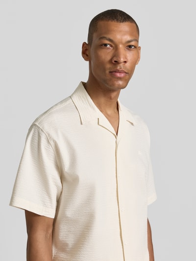 Männermodel trägt Relaxed Fit Freizeithemd aus reiner Baumwolle von Lacoste in Creme mit Crinkle-Textur, Resortkragen, Nahaufnahme Oberkörper.