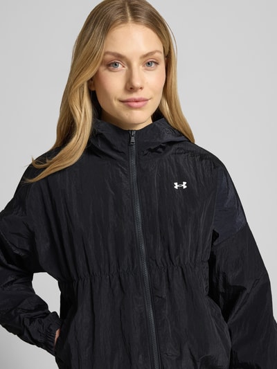 Frauenmodel trägt Jacke mit Kapuze und Logo von Under Armour in Schwarz, Regular-Fit, Reißverschluss, Nahaufnahme Oberkörper, Rückenlänge 57 cm, Schulterbreite 66 cm, Brustweite 64 cm, Ärmellänge 51 cm.