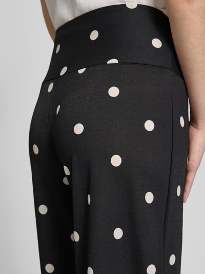 Vrouwenmodel draagt Wide Leg Pants uit viscosemix met zijritssluiting van Gina Tricot, zwarte stof met witte polkadots, detailopname rug.