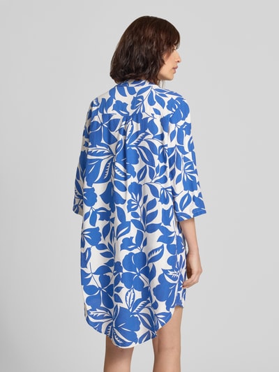 Frauenmodel trägt Minikleid aus Viskose-Mix mit verlängertem Rücken von ZABAIONE in Weiß-Blau mit floralem Muster, lockere Passform, Ganzkörperansicht Rückansicht. Modell Ma4rtaa, Serafino-Kragen, 1/2-Arm, abgerundeter Saum, Rückenlänge 98 cm bei Größe S, Brustweite 57 cm, Ärmellänge 42 cm.