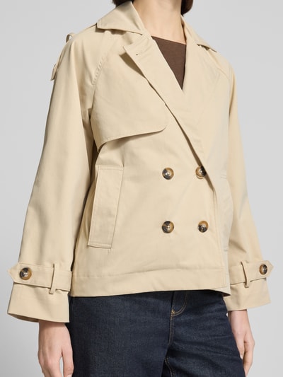 Modelka kobieca nosi Trenchcoat mit Ärmelriegeln Modell 'AMONA' od B.Young, beżowy, krój regular fit, dwurzędowy, kieszenie, kołnierz wykładany, szerokość w rozmiarze 36: 52 cm, długość tyłu: 63 cm, długość rękawa: 46 cm, szerokość ramion: 46 cm, gładka tekstura, widok z przodu, ujęcie półpostaciowe