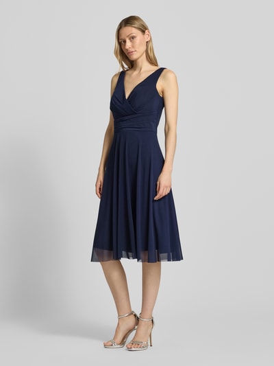 Frauenmodel trägt Cocktailkleid in Wickel-Optik mit V-Ausschnitt von TROYDEN COLLECTION, Mesh, taillierter Schnitt, Midikleid, ganzkörperansicht von vorne.
