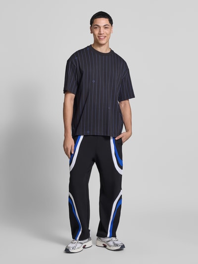 Männermodel trägt Relaxed Fit Sweatpants aus Baumwoll-Mix Modell 'Nalotron' von Hugo Blue in Schwarz mit Kontraststreifen, Ganzkörperansicht von vorne.