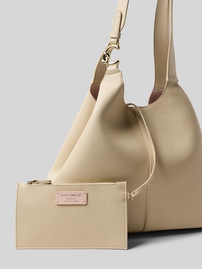 Produktfoto, Handtasche mit Tragehenkel von Coccinelle in Beige, Hauptfach mit Magnetverschluss, Label-Detail, Maße: 34 cm Breite, 29 cm Länge, 14 cm Tiefe, Schulterriemen 50 cm, strukturierte Oberfläche