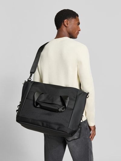 Männermodel trägt zwarte Weekend Bag met logo-Detail Model 'Otaru' van Rains, Hoofdvak met ritssluiting, afneembare schouderband, breedte 54 cm, lengte 38 cm, diepte 20 cm, bandlengte 86 cm, Ganzkörperansicht Rückansicht