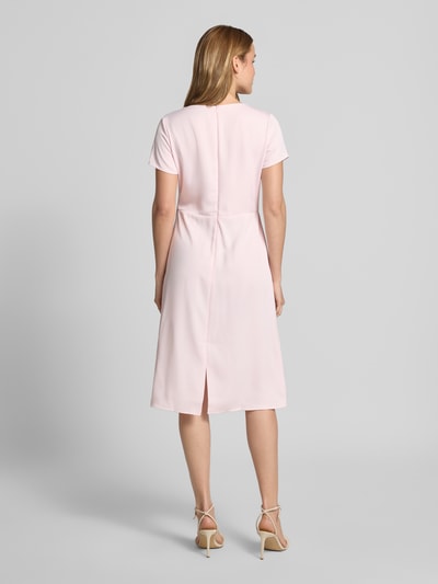 Frauenmodel trägt Knielanges Cocktailkleid mit Knotendetail und Reißverschluss von Rinascimento in zartem Rosa, Taillierter Schnitt, Knielänge, Rundhalsausschnitt, rückseitiger Reißverschluss, glatte Textur, Rückenlänge bei Größe S 105 cm, Brustweite 46 cm, Ärmellänge 17 cm, Ganzkörperansicht Rückansicht.