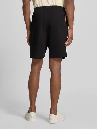 Männermodel trägt Shorts mit elastischem Bund und Logo von EA7 Emporio Armani in Schwarz, Regular Fit, Baumwolle, Ganzkörperansicht Rückansicht.