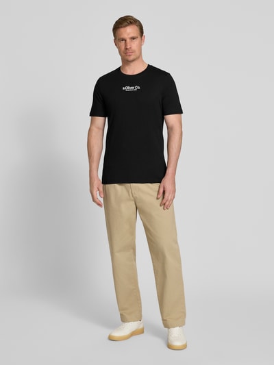 Mężczyzna nosi Regular Fit T-Shirt aus reiner Baumwolle od s.Oliver RED LABEL, czarny, jednolity kolor, krótki rękaw, okrągły dekolt, aplikacja z logo, jersey, widok całej sylwetki z przodu.