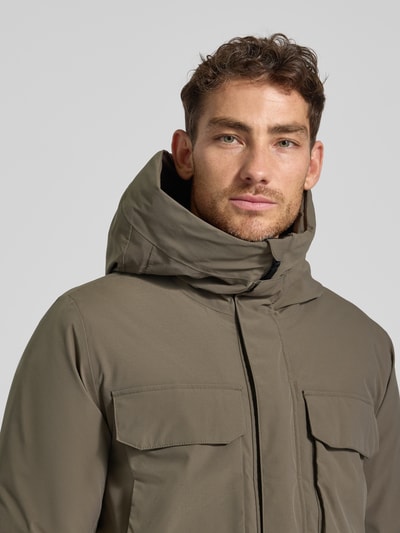 Męski model nosi Parka z patkami model 'AIDEN' od Didriksons, khaki, gładka faktura, regular fit, kaptur, zbliżenie na górę ciała.