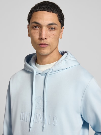 Männermodel trägt Hoodie aus Baumwoll-Mix Modell 'FREDERIKS' von JACK & JONES in Hellblau mit Label-Print, Nahaufnahme Oberkörper.