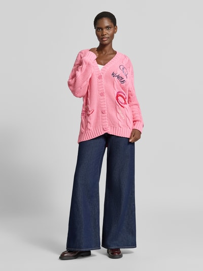 Vrouwenmodel draagt cardigan met Motief-Stitchings en V-hals van Milano Italy, katoenmix, loose fit, knoopsluiting, ruglengte maat S 74 cm, mouwlengte 57 cm, roze met breitekstuur, Ganzkörperansicht van voren.