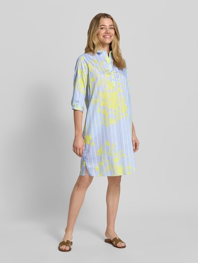 Frauenmodel trägt knielanges Hemdblusenkleid mit kurzer Knopfleiste von Milano Italy in Reine Baumwolle, Gerader-Schnitt, Hemdblusenkragen, 1/2-Arm, Rückenlänge 99 cm, Brustweite 51 cm, Ärmellänge 42 cm, hellblau mit gelbem Muster; Ganzkörperansicht von vorne.