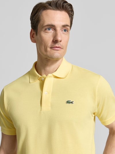 Męski model nosi Regular Fit Poloshirt aus reiner Baumwolle von Lacoste, efekt: jednolity kolor, krój regular fit, wyhaftowane logo, kołnierzyk polo, krótki rękaw, prążkowane zakończenia, boczne rozcięcia, wykończenie: pika, materiał: bawełna, jasny żółty, zbliżenie na górną część ciała