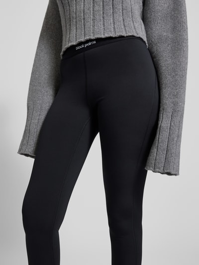 Frauenmodel trägt Leggings mit elastischem Logo-Bund von black palms, schwarzer Material-Mix mit Stretch-Anteil, körpernaher Schnitt, Nahaufnahme Oberkörper.