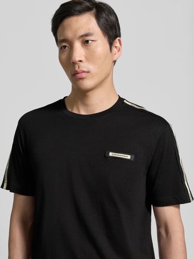 Mężczyznamodel nosi Regular Fit T-Shirt mit Logo-Patch od EA7 Emporio Armani z bawełny, okrągły dekolt, długość tyłu 52 cm, Nahaufnahme Oberkörper.