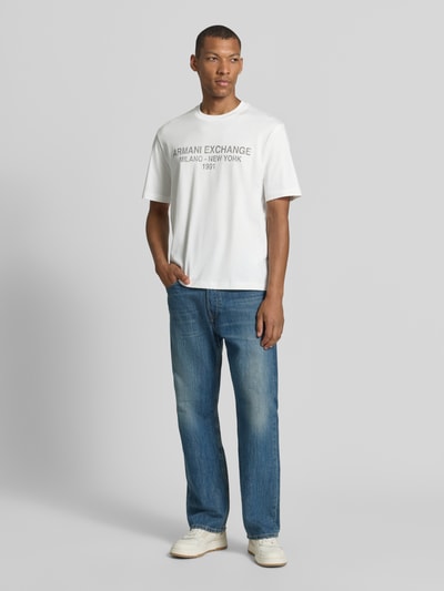 Männermodel trägt T-Shirt mit Label-Print und Rundhalsausschnitt von Armani Exchange, weiße Baumwolle, lockerer Schnitt, Ganzkörperansicht von vorne.
