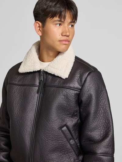 Männermodel trägt Bomberjacke mit Kentkragen und gerippten Abschlüssen von Alpha Industries in Schwarz, Kunstleder-Optik, Nahaufnahme Oberkörper. Regular Fit, Teddyfell am Kragen, Reißverschluss, Eingrifftaschen mit Druckknopf, Rückenlänge 66 cm, Schulterbreite 48 cm, Brustweite 55 cm, Ärmellänge 70 cm.