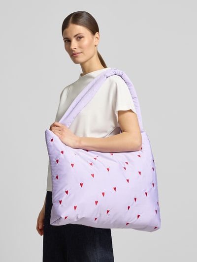 Frauenmodel trägt Tote Bag mit Allover-Motiv-Stitching Modell 'Puffy' von STUDIO NOOS in Flieder mit roten Herz-Stickereien, Ganzkörperansicht von vorne. Breites, offenes Hauptfach, gesteppt, Tragehenkel, Maße 57x42x9 cm, Schulterriemen 73 cm.