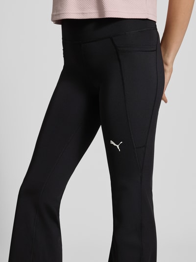 Frauenmodel trägt schwarze Slim Fit Sport-Leggings mit Logo-Print Modell 'TAD ESSENTIAL' von PUMA, Damen Sport-Leggings, Nahaufnahme Oberschenkel.