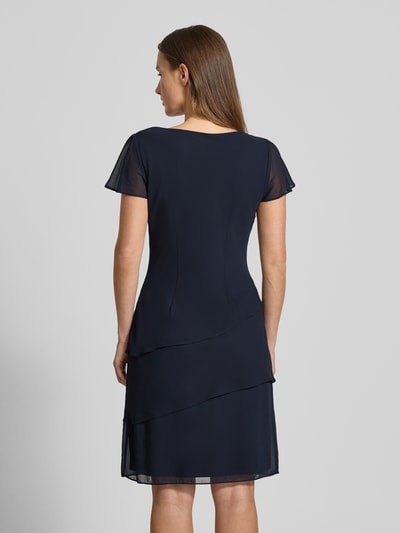 Kobiece modelka nosi tailliertes Cocktailkleid mit Volants od Christian Berg Cocktail w kolorze granatowym, tkanina gładka, lekko połyskująca, całkowity widok z tyłu. Kontekst: dopasowany krój, dekolt wodospadowy, rękawy z falbaną, boczny zamek, długość tyłu 95 cm, szerokość w biuście 39 cm, długość rękawa 15 cm dla rozm. 36.