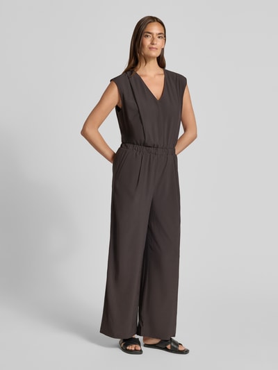 Modelka nosi Relaxed Fit Jumpsuit mit V-Ausschnitt Modell 'Charlou' od Someday, elastyczna mieszanka materiałów, ciemny kolor, wpuszczane kieszenie, taliowany krój, bez rękawów, szerokie nogawki, całkowita długość 146 cm, długość tyłu 44 cm, szerokość w rozmiarze 36: 52 cm, długość wewnętrzna nogawki 71 cm, widok całej sylwetki z przodu.