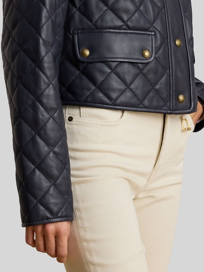 Frauenmodel trägt Cropped Lederjacke aus reinem Lammleder von Lauren Ralph Lauren in Dunkelblau, gestepptes unifarbenes Material, Pattentaschen, Nahaufnahme Oberkörper.