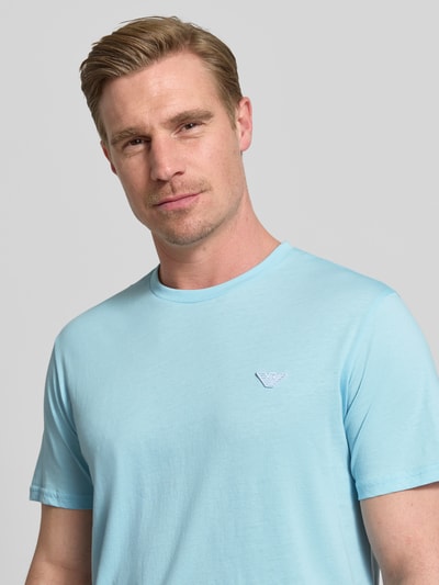 Männermodel trägt T-Shirt mit Logo-Patch und Rundhalsausschnitt von Emporio Armani in Hellblau, Reine Baumwolle, Modern Fit, Nahaufnahme Oberkörper. Rückenlänge bei Größe M: 69 cm.