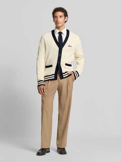 Männermodel trägt Regular Fit Strickjacke aus reiner Baumwolle von GANT in Creme mit dunkelblauen Details, Ganzkörperansicht von vorne.