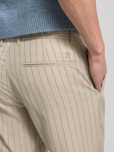 Mężczyzna nosi Stoffhose mit französischen Eingrifftaschen od Les Deux, beżowe w paski, kieszenie z tyłu, regular fit, zbliżenie na biodra.