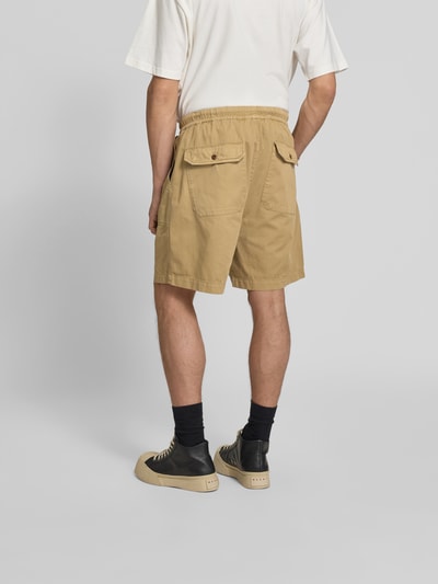 Männermodel trägt Bermudas aus reiner Baumwolle von Officine Générale in Beige mit elastischem Bund und Eingrifftaschen, Ganzkörperansicht Rückansicht.