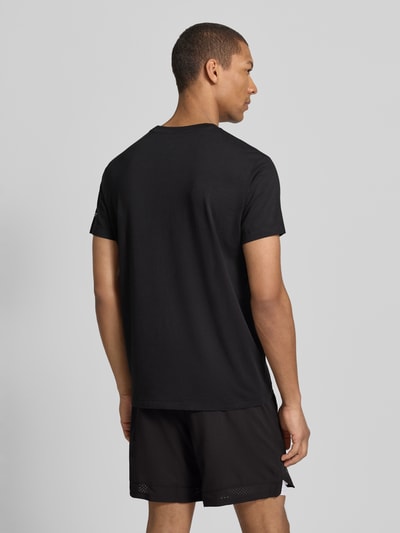 Męski model ma na sobie Regular Fit T-Shirt mit Logo-Print von Fabletics z elastycznej mieszanki bawełny, czarny kolor, krój regular fit, nadruk logo, okrągły dekolt, długość tyłu w rozmiarze M: 65 cm, całkowity widok z tyłu.