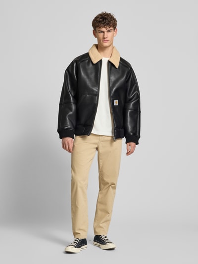 Männermodel trägt Bomberjacke mit Zweiwege-Reißverschluss Modell 'SHEPTON' von Carhartt Work In Progress in Schwarz und Beige, Relaxed Fit, Umlegekragen mit Teddyfell, Eingrifftaschen, Label-Detail, Ganzkörperansicht von vorne.
