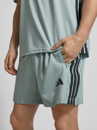 Männermodel trägt Shorts mit elastischem Bund von adidas Training in Hellblau mit Label-Print, Reißverschlusstaschen, Nahaufnahme Oberkörper.