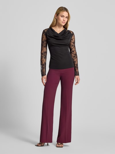 Kobiece model prezentuje Slim Fit Longsleeve mit Spitzenbesatz od Rinascimento, czarny, obszycie koronką, półprzezroczysty materiał, lejący kołnierz, długość tyłu w rozmiarze S: 60 cm, pełen widok z przodu.