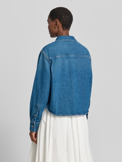 Frauenmodel trägt Relaxed Fit Jeansbluse mit Knopfleiste Modell 'CELIA' von Samsøe Samsøe aus reiner Baumwolle, mittleres Blau, lockerer Schnitt, Hemdblusenkragen, glatte Textur, Rückenlänge 60 cm, Ärmellänge 62 cm, Ganzkörperansicht Rückansicht.