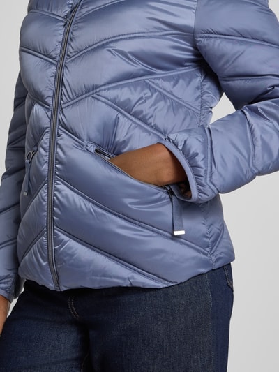 Vrouwenmodel draagt Steppjacke mit Stehkragen und Reißverschlusstaschen van Christian Berg Woman Selection in regular fit, licht glanzende blauwe stof, rits- en steekzakken, taille op heuplengte, Nahaufnahme bovenlichaam, ruglengte 61 cm, schouderbreedte 42 cm, borstwijdte 51 cm, mouwlengte 58 cm.