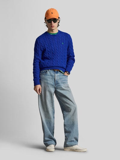 Męski model nosi Regular Fit Strickpullover aus reiner Baumwolle von Polo Ralph Lauren, efekt: jednolity kolor, dzianina w warkocze, detal z logo marki, okrągły dekolt, długi rękaw, prążkowane zakończenia, sweter z bawełny, imitacja dzianiny, wykończenie materiału: dzianina; widok całej sylwetki z przodu.