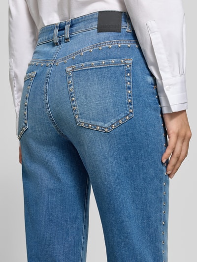 Frauenmodel trägt Slim Fit Jeans aus Baumwoll-Mix mit Nietenbesatz von Marc Cain, mieszanka bawełny, krój slim fit, obszycie nitami, skrócony krój, 5 kieszeni, zapięcie na guzik i zamek błyskawiczny, Szerokość w rozmiarze 36: 40 cm, Długość wewnętrzna nogawki w rozmiarze 36: 72 cm, Ganzkörperansicht Rückansicht.