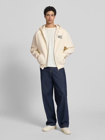 Männermodel trägt Oversized Sweatjacke mit Logo-Stitching von KARL KANI aus Baumwoll-Mix in Creme, Kapuze, Kängurutasche, Reißverschluss, Ganzkörperansicht von vorne.